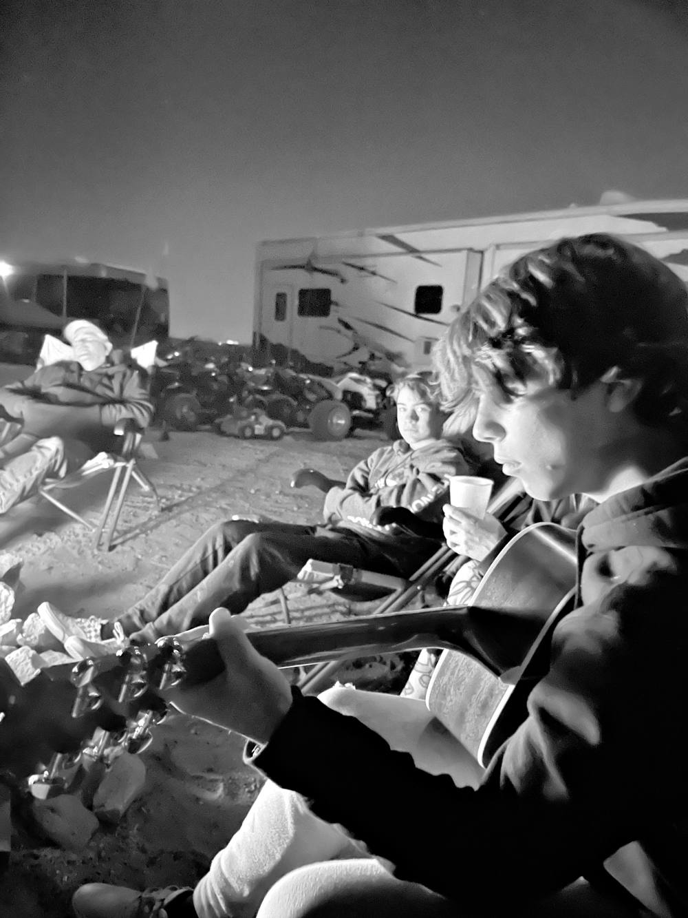 Friends gathered around a campfire playing guitar